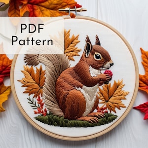 May include: Embroidered hoop art featuring a brown squirrel holding a red berry, surrounded by autumn leaves in shades of orange, yellow, and green. The hoop is made of wood and has a white fabric background. The text "PDF Pattern" is displayed in a white box at the top of the image.