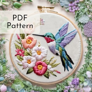 Puede incluir: Arte de bordado en aro con un colibrí colorido con un pico largo, posado en una rama con flores rosas, blancas y verdes. El aro es de madera y tiene un acabado natural. El bordado se realiza con una variedad de puntadas y colores, creando una imagen realista y detallada.