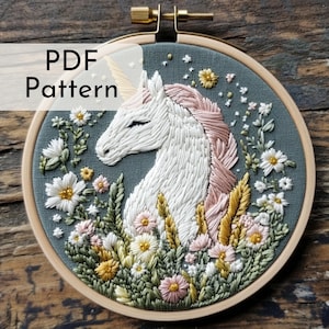 May include: Embroidered unicorn design in a wooden hoop. The unicorn has a white body, pink mane, and golden horn, surrounded by colourful flowers and greenery. The text "PDF Pattern" is visible.