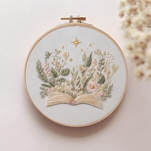 Floral Book Embroidery Pattern featuring an open book surrounded by delicate pastel flowers and soft glowing stars. This dreamy and cozy design is perfect for book lovers, reading corner decor, and those who enjoy peaceful, aesthetic embroidery projects. Ideal as a handmade gift for literary fans or anyone who loves gentle, pastel artwork. Includes 6 hoop sizes and easy instructions for all skill levels.