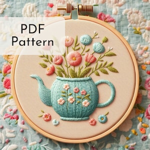 Op de afbeelding: Een PDF-patroon voor borduurwerk met een theepot met een boeket roze, blauwe en groene bloemen. De theepot is blauw en wit met een bloemenpatroon. De bloemen zijn in een vaasvormige vorm gerangschikt.