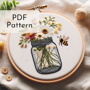 May include: A white embroidery hoop featuring a floral arrangement in a glass jar. The flowers are white, yellow, and red. A bee is flying above the jar. The text "PDF Pattern" is in the top left corner of the image.
