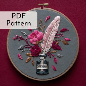 Puede incluir: Arte de aro bordado con una pluma, flores y un tintero. El diseño incluye una gran pluma rosa, una peonía rosa y hojas burdeos, todo sobre un fondo gris. Se muestra el texto "PDF Pattern".