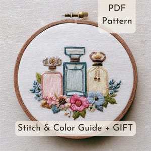 Puede incluir: Un bastidor de bordado con una pieza de tela que muestra frascos de perfume bordados en rosa, azul y amarillo, rodeados de coloridos detalles florales. El texto PDF Pattern y Stitch & Color Guide + GIFT es visible en la imagen.