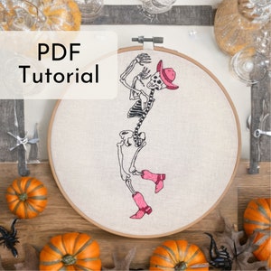 Peut inclure: Art de broderie sur un cercle représentant un squelette portant un chapeau de cowboy rose et des bottes. Le cercle est blanc avec un fond beige. Le texte "PDF Tutorial" est visible dans le coin supérieur gauche de l'image.