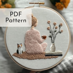 Könnte beinhalten: Stickbild in einem Stickrahmen mit einer Frau in einem rosa Pullover, die mit einer Katze und einer Tasse Kaffee sitzt. Die Frau ist von einem braunen Teppich und einer Vase mit Blumen umgeben. Der Text "PDF Pattern" befindet sich in der oberen linken Ecke des Bildes.