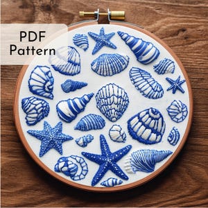 May include: Embroidered hoop art featuring a variety of blue and white seashells and starfish on a white background. The hoop is made of wood and has a natural finish.
