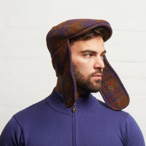 May include: A patterned wool cap with ear flaps. The cap is brown, orange, and purple with a geometric pattern. The ear flaps are attached with buttons.