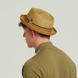 Può includere: Un cappello fedora di colore beige e marrone con una fascia blu scuro. Il cappello è fatto di paglia e ha un'ampia tesa.