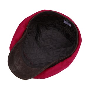 May include: A red wool newsboy cap with a brown suede brim. The cap has a quilted lining.