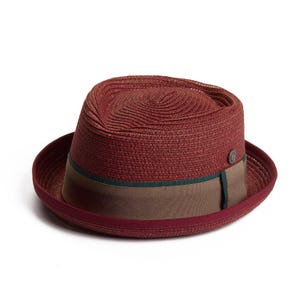 Può includere: Un cappello fedora color borgogna con una fascia marrone e verde. Il cappello è fatto di paglia intrecciata.