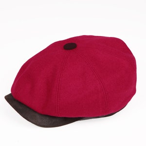 May include: A red wool newsboy cap with a brown leather brim.