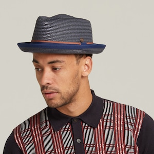 May include: A dark blue fedora hat with a brown band and a navy blue underbrim. The hat is made of woven straw.
