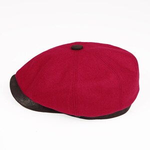May include: A burgundy wool newsboy cap with a brown leather brim.
