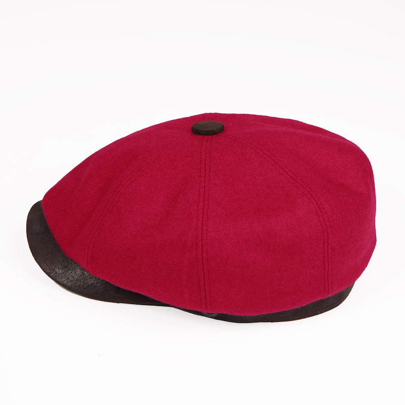 May include: A burgundy wool newsboy cap with a brown leather brim.