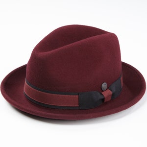 Op de afbeelding: Een bordeauxrode fedora-hoed met een zwart en bordeauxrode band.