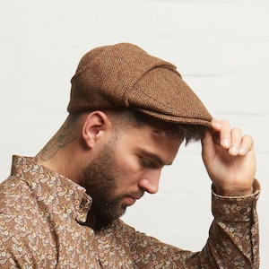 Op de afbeelding: Bruine visgraat tweed flat cap. De pet heeft een klassiek ontwerp met een afgeronde kroon en een korte, stijve klep. De stof heeft een textuur. Een stijlvol accessoire.