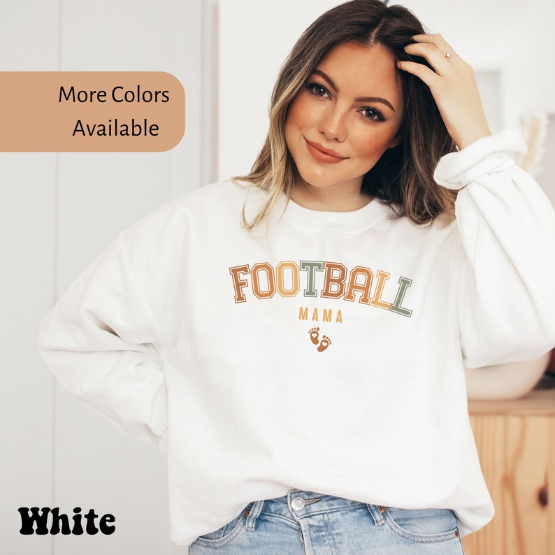 May include: White sweatshirt with the text "FOOTBALL MAMA" in a retro font, with baby footprints below. The sweatshirt also has the text "More Colors Available" and "White".