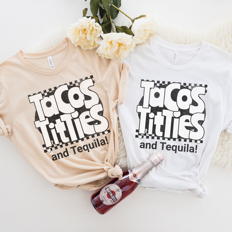 May include: Two white t-shirts with the text "Tacos Titties and Tequila!" printed in black. The shirts are laid out on a white surface with a bottle of sparkling wine.