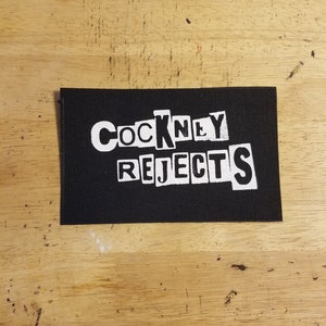 Può includere: Toppa in tessuto nero con lettere bianche che recitano "Cockney Rejects".