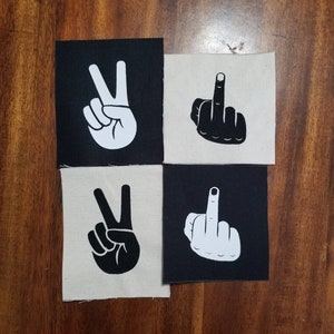 May include: Four iron-on patches, two with a white peace sign on a black background and two with a black middle finger on a white background.