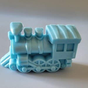 May include: A light blue plastic toy train engine with a black window and wheels. The train has a rounded top and three smokestacks.