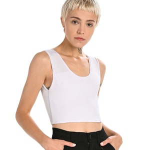 Puede incluir: Un top blanco sin mangas y corto con cuello redondo. El top se lleva con pantalones negros y una cadena plateada.