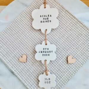 May include: White ceramic flower-shaped ornaments with the text "Azalea Rue Baines", "9th January 2024", and "7lb 5oz".