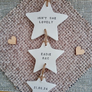 May include: A set of three white ceramic stars with twine hanging from each. The top star says "Isn't she lovely", the middle star says "Eadie Mac", and the bottom star says "21.06.24".