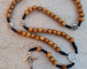 Può includere: Un rosario di legno con cordino nero e dettagli in metallo argentato. Il rosario include un crocifisso con una figura di Gesù Cristo.