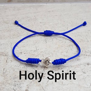 Op de afbeelding: Een blauw koordarmband met een zilveren duivenbedel. De armband heeft een schuifknoop sluiting en de woorden "Holy Spirit" zijn onder de armband gedrukt.
