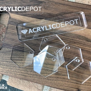 May include: A set of clear acrylic hexagon shapes with holes for hanging. The shapes are on a wooden surface with the text "ACRYLICDEPOT" on a larger rectangular piece of acrylic.