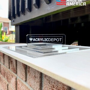 May include: A clear acrylic display stand with three tiers. The stand is made in the USA and features the logo "ACRYLICDEPOT" on the top tier.
