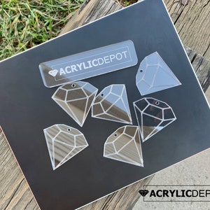 May include: A set of six clear acrylic diamond-shaped ornaments with a hole at the top for hanging. The ornaments are on a black surface with the text "ACRYLICDEPOT" printed on a white rectangle.