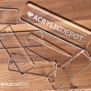 May include: A stack of clear acrylic rectangular name tags with rounded corners. The top tag has the text "ACRYLICDEPOT" and a diamond symbol.