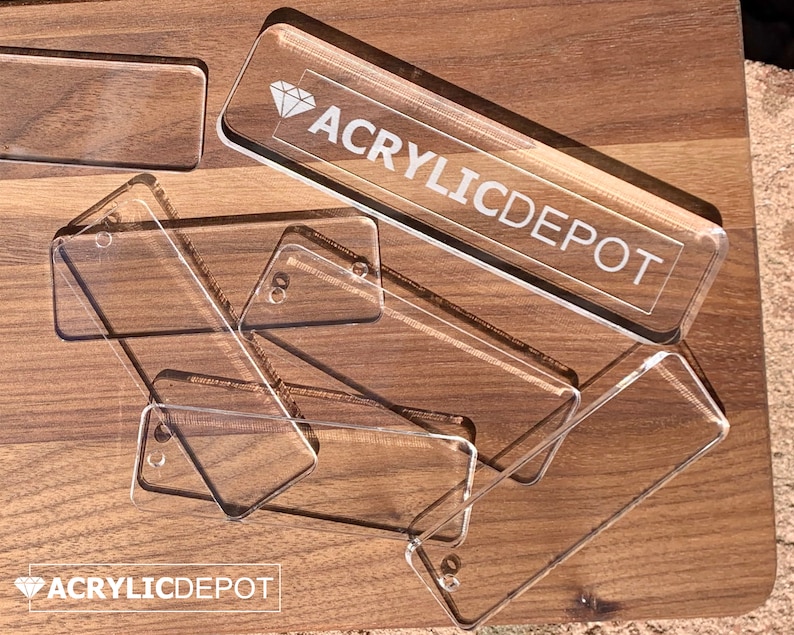 May include: A stack of clear acrylic rectangular name tags with rounded corners. The top tag has the text "ACRYLICDEPOT" and a diamond symbol.