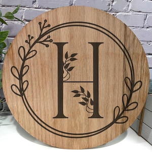 May include: A wooden round sign with a decorative floral design and the letter "H" in the center.
