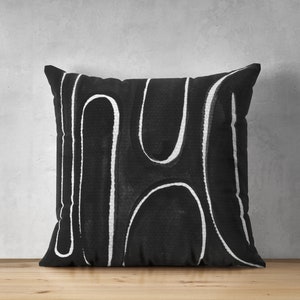 May include: Black and white throw pillow with an abstract design of white lines on a black background.