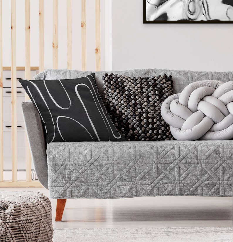 May include: A gray sofa with a quilted cover and three throw pillows. The pillows are black with white abstract lines, gray with a textured surface, and a light gray knotted pillow.