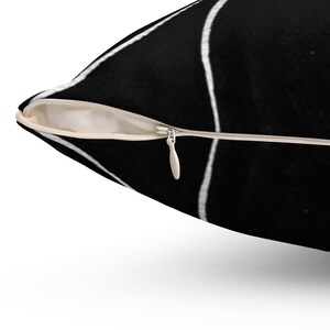 May include: A black and white throw pillow with a geometric pattern. The pillow has a zipper closure.