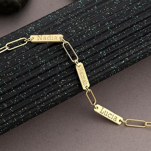 May include: Gold chain bracelet with two personalised name tags. The tags are rectangular and have the names "Nadia" and "Lucia" engraved on them.