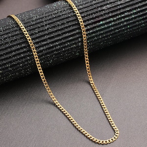 Könnte beinhalten: Eine goldene Halskette mit einem Curb-Gliederketten-Stil. Die Kette liegt auf einer schwarzen Oberfläche.