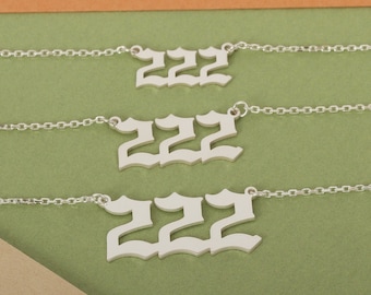 May include: Three silver necklaces with the number 222 in a gothic font. The necklaces are layered on top of each other, with the largest necklace on the bottom and the smallest necklace on the top.