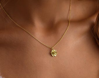 May include: A delicate gold chain necklace with a small flower pendant. The flower has a textured design and a single diamond in the center.