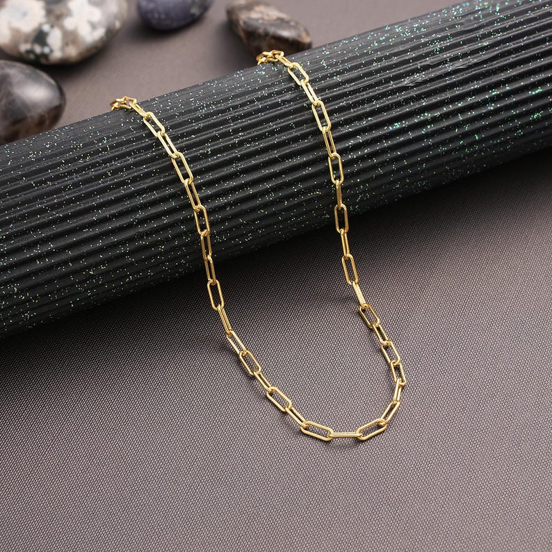 May include: A gold chain necklace with a delicate, linked chain design. The chain is made of small, rectangular links.