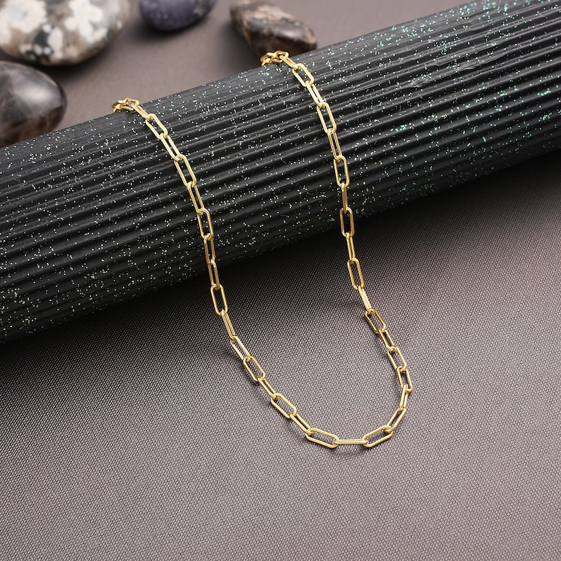 May include: A gold chain necklace with a simple, linked design. The chain is made of small, rectangular links.
