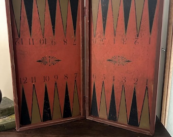 May include: An open, antique backgammon board with a red background and alternating black and gold triangles. The board has a dark brown wooden frame and is numbered 1-12 on each side. Decorative flourishes are present.