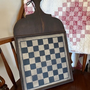 Puede incluir: Un tablero de damas de madera con un patrón de tablero de damas blanco y negro. El marco es de color marrón oscuro y tiene un asa en la parte superior.