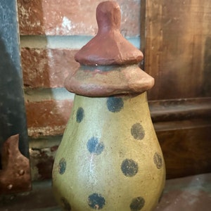 May include: A brown and green ceramic jar with a red lid and black polka dots.