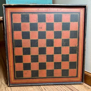 Può includere: Una scacchiera di legno vintage con un motivo a scacchiera rosso e nero. La scacchiera è incorniciata da una cornice in legno scuro con una bordura dorata.